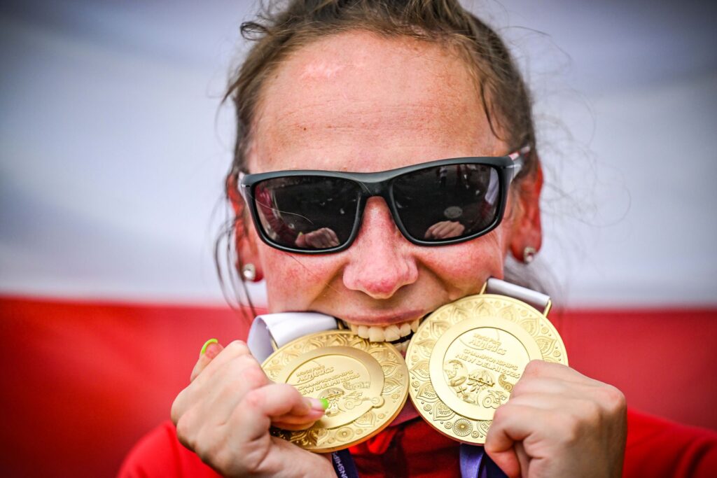 Uśmiechnięta Magdalena Andruszkiewicz przygryza swoje dwa złote medale