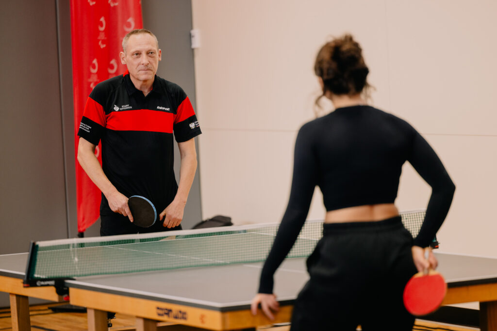 Mężczyzna i kobieta stoją po obu stronach stołu do tenisa stołowego tuż przed grą