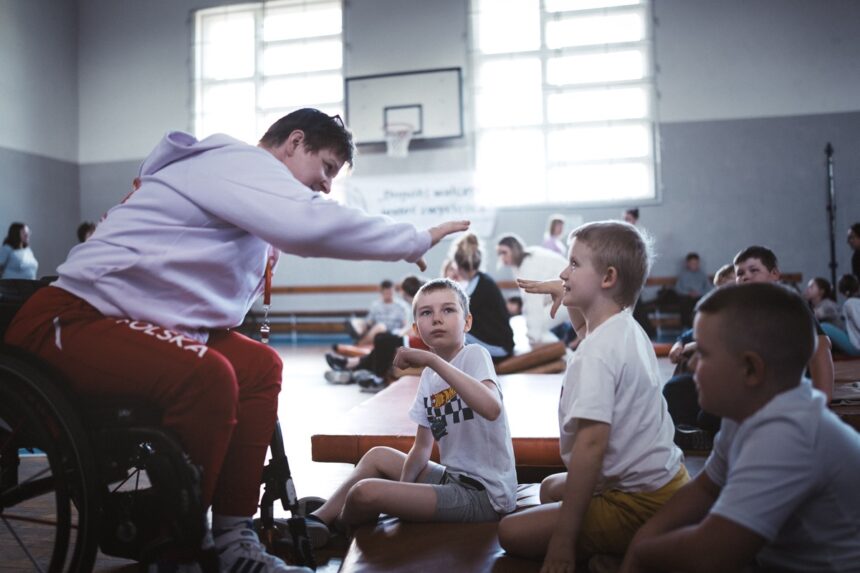 Lucyna Kornobys prezentuje ruch ręką dzieciom w sali gimnastycznej