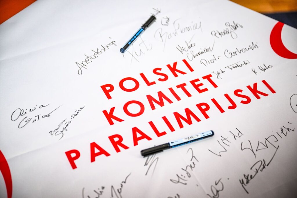 Flaga Polskiego Komitetu Paralimpijskiego z podpisami zawodników, trenerów i członków misji paralimpijskiej