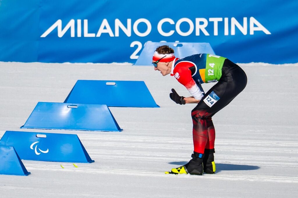 Witold Skupień na trasie biegu narciarskiego. W tle banda z napisem: Milano Cortina 2026