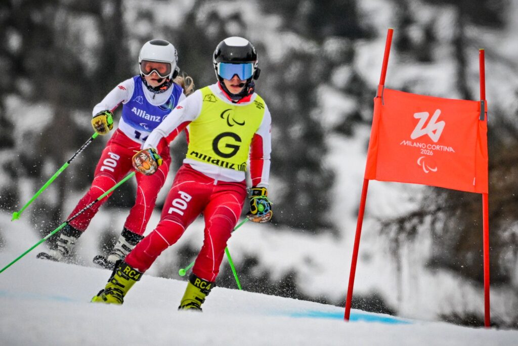 Oliwia Gołaś jedzie za swoim przewodnikiem Andrzejem Stasikiem na nartach po śniegu, mijając bramkę slalomową