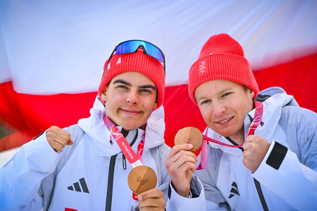 Michał Gołaś i Kacper Walas prezentują swoje brązowe medale. W tle polska flaga