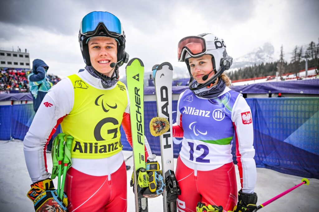 Andrzej Stasik i Oliwia Gołaś pozują do zdjęcia w strojach narciarskich, trzymając narty