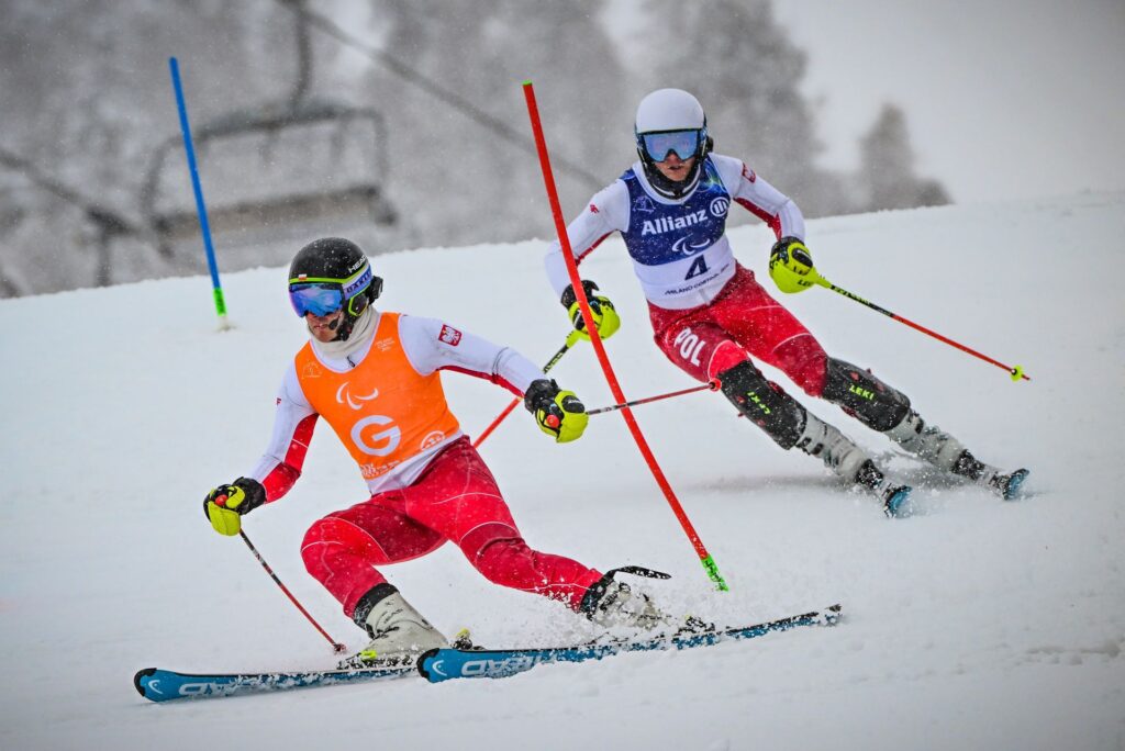 Michał Gołaś jedzie na nartach po stoku, mijając tyczkę slalomową, za swoim przewodnikiem, Kacprem Walasem