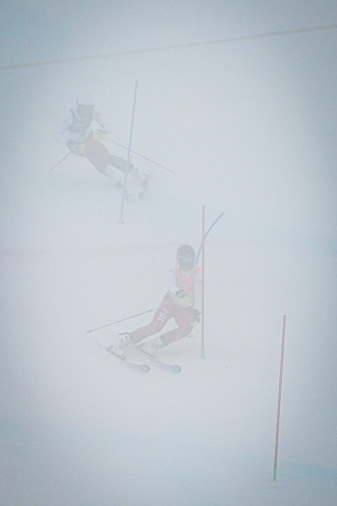 Zamglony widok na mijających na trasie tyczki slalomowe polskich zawodników